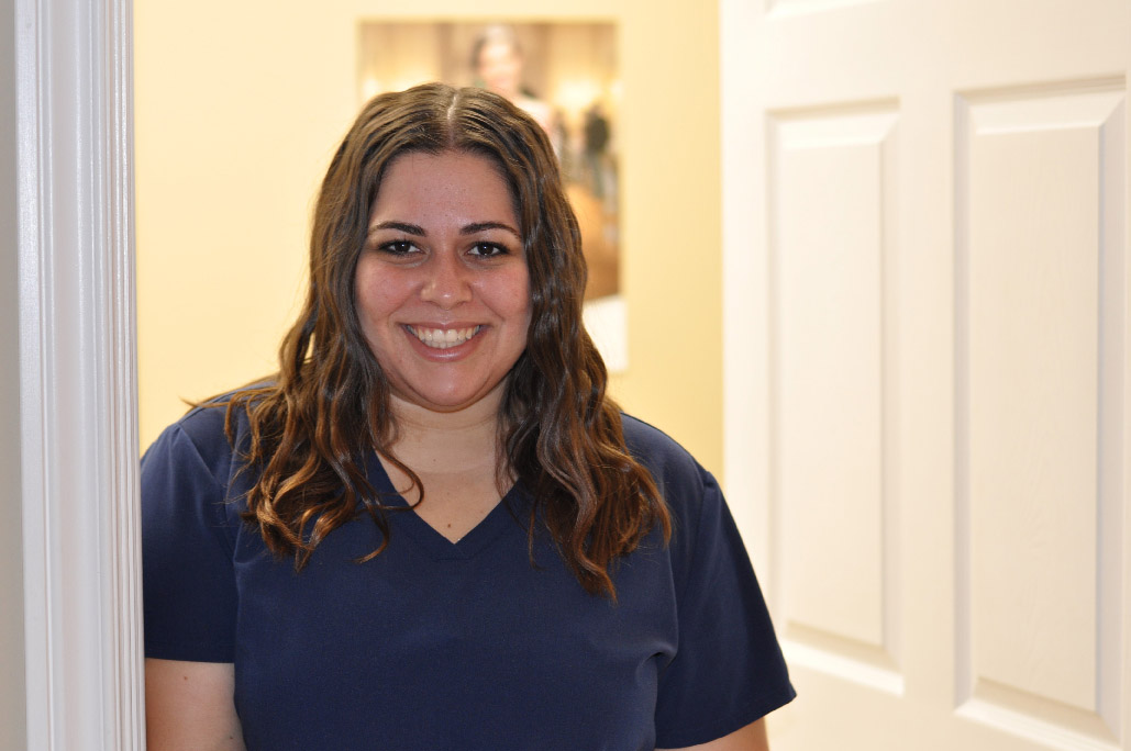 Natasha Fidalgo, certified dental assistant, wearing navy blue scrubs in front of a white door at Karen Archer DDS in Leamington, ON