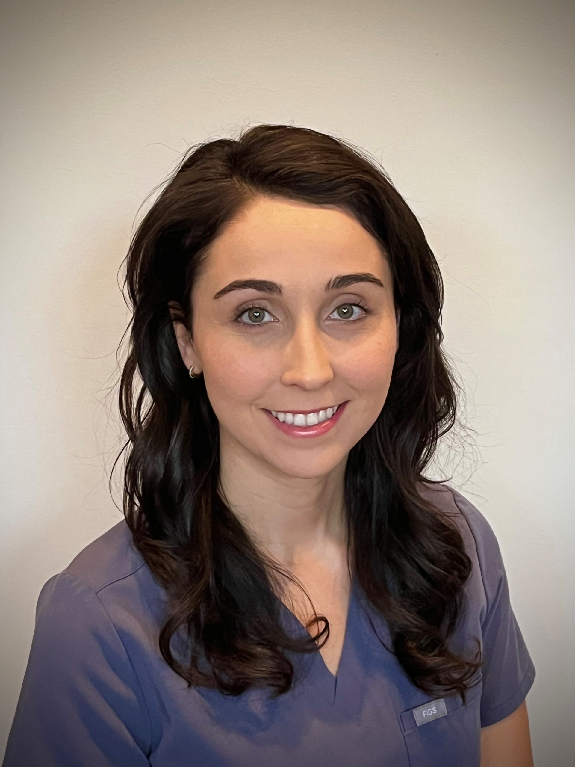 Dr. Valerie Spano, DDS at Karen Archer DDS in Leamington, ON, wearing gray scrubs in front of a white wall 